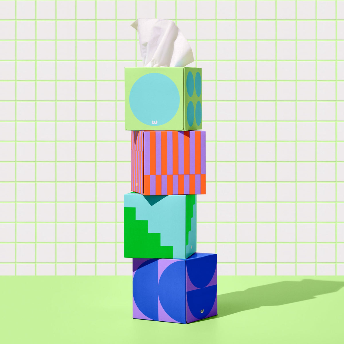 Four Who Gives a Crap tissue boxes stacked on top of each other against green and white bathroom wall